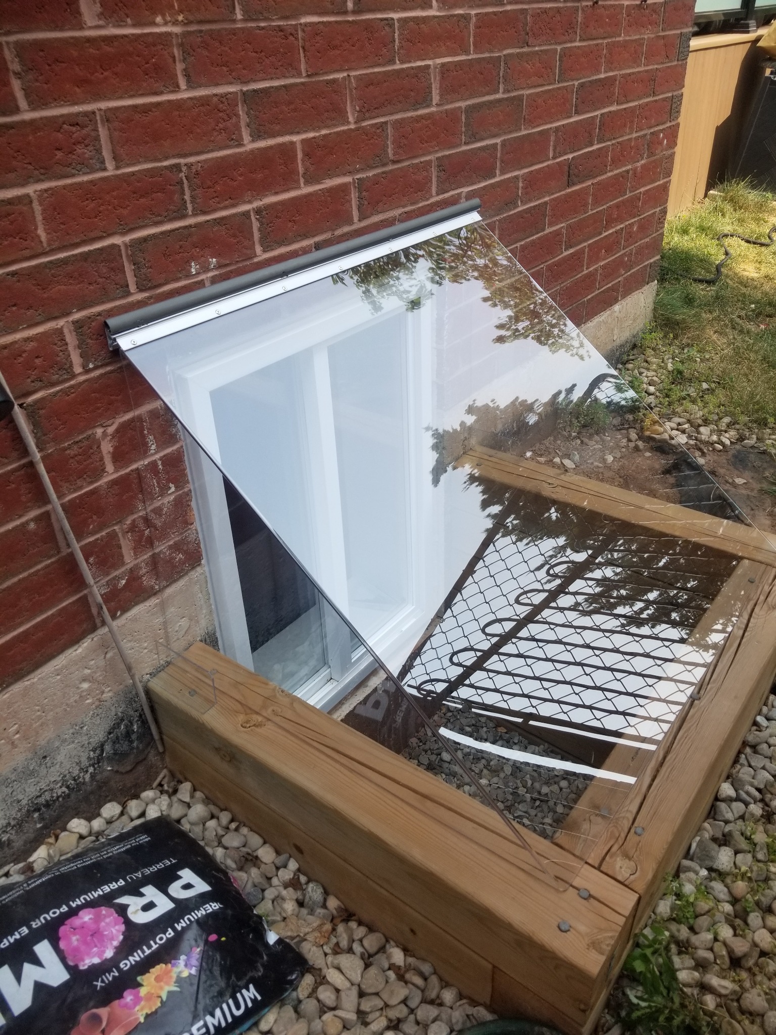 Clear sloped polycarbonate window well cover installed on a Toronto-area home